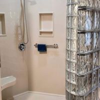 Solid surface wall panels and grab bars and niches around a curved glass block wall - Innovate Building Solutions