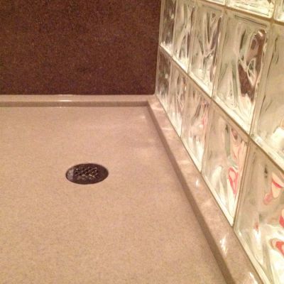 Round drain in a bone colored solid surface shower pan for glass blocks- Innovate Building Solutions