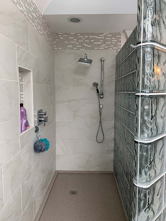 Square drain in solid surface shower base with a curved glass block shower wall on top - Innovate Building Solutions