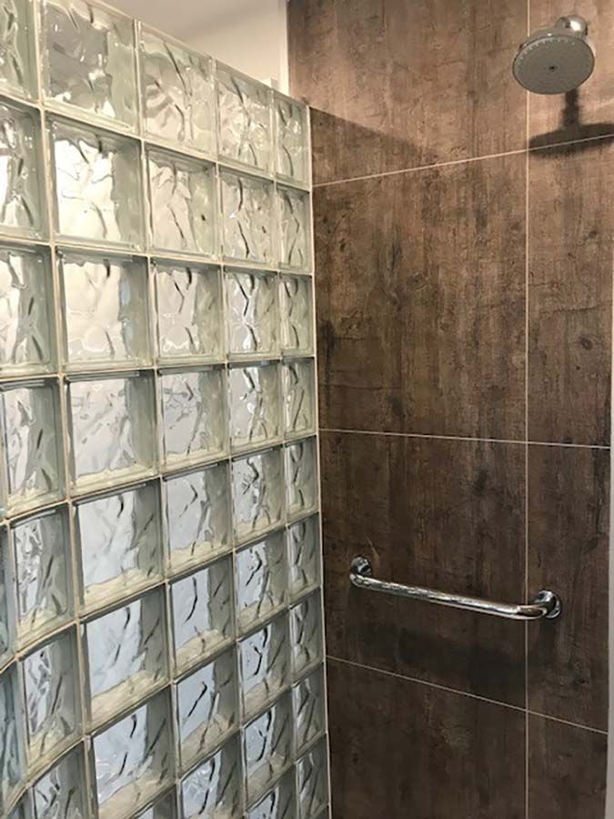 Rough wood laminate panels with grab bar in a premade glass block shower - Innovate Building Solutions 