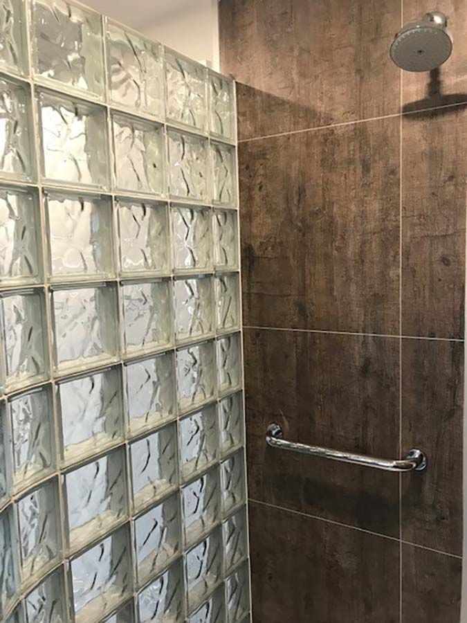 Rough wood laminate panels with grab bar in a premade glass block shower - Innovate Building Solutions